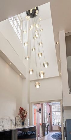 a large open living room and kitchen area with modern lighting fixtures hanging from the ceiling