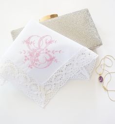 two napkins with pink designs on them next to some gold earrings and a pair of scissors