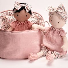 two dolls sitting next to each other in a pink basket with flowers on it,