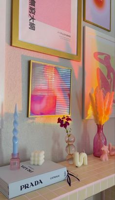 there are two framed pictures on the wall above a table with flowers and candles in vases