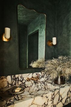 a bathroom with marble counter tops and green walls, gold fixtures on the mirror above it