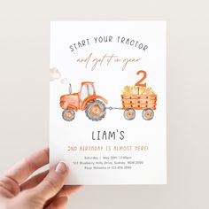 a hand holding up a birthday card with an orange tractor and number two on it