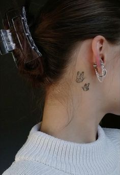 a woman with a butterfly tattoo on her left side behind the ear, wearing a white sweater