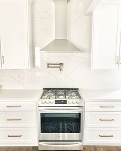 a white kitchen with marble counter tops and stainless steel stove top oven in the middle