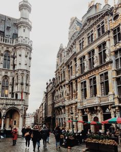 people are walking down the street in an old european city with tall buildings on either side