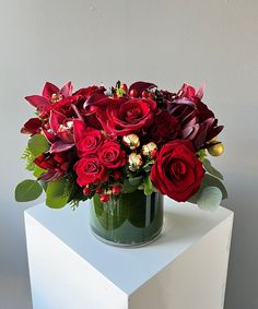 a green vase filled with red flowers on top of a white table next to a wall