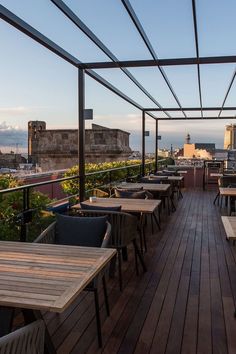 an outdoor dining area with wooden tables and chairs, overlooking the city in the distance