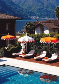 an outdoor pool with lounge chairs and umbrellas next to the water's edge