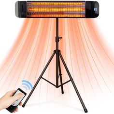 a person holding a remote control next to an electric heater on a tripod