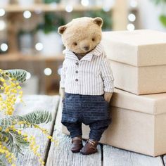 a small teddy bear is standing next to some boxes on a wooden table with yellow flowers in the background