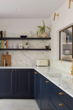 a kitchen with blue cabinets and marble counter tops, gold faucets and open shelving