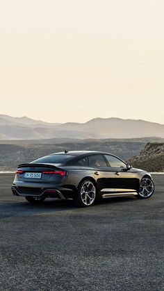 the rear end of a black sports car driving on a road with mountains in the background