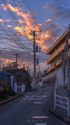 an empty street with power lines above it and buildings in the background at sunset or dawn