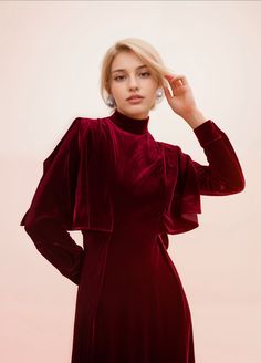 a woman in a red dress posing for the camera with her hand on her head