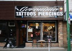 the front of a tattoo shop with signs on it's windows and two chairs outside