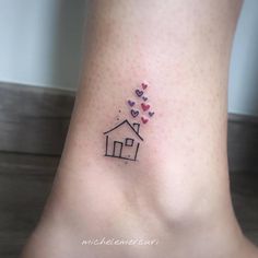 a small tattoo on the ankle of a woman with hearts flying out of her house