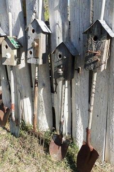 there are many bird houses hanging on the wooden fence with shovels next to them