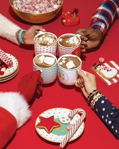 people holding hands at a table filled with hot chocolates and marshmallows