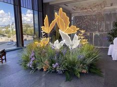 an arrangement of flowers in the middle of a room with large windows and white chairs