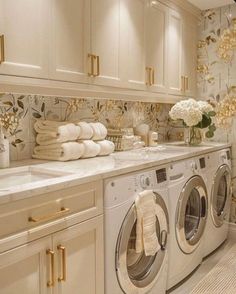 a washer and dryer in a room with white cabinets, gold handles and flowers on the wall