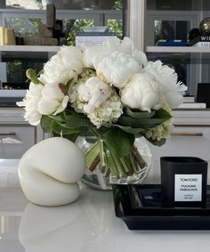 a vase filled with white flowers sitting on top of a table next to a candle