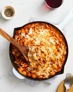 a skillet filled with pasta and cheese on top of a table next to two spoons