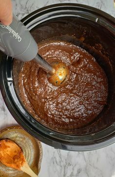 a person mixing chocolate in a crock pot with a spatula on the side