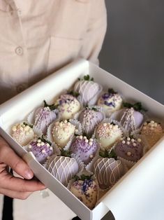 a person holding a box full of chocolates with white and purple frosting on them