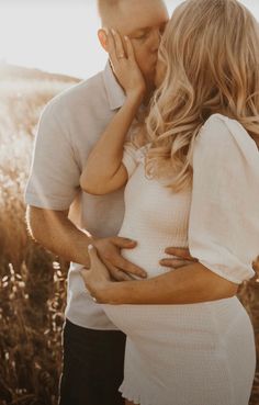 a man and woman kissing while standing in tall grass with the sun shining on them