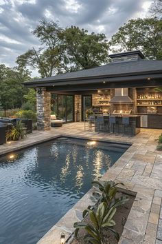 an outdoor kitchen next to a pool in the middle of a yard with lights on