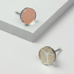 two silver and gold cufflinks sitting on top of a white box next to each other