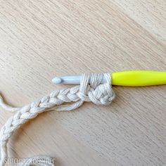 a yellow crochet hook is hooked up to a white rope on a wooden surface