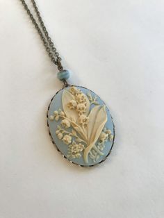 "Here is a beautiful blue lily of the valley cameo necklace. This is a large cameo which features nicely detailed lily of the valley flowers against a dreamy blue background. This cameo is set in an oxidized brass setting and is suspended from one Czech glass bead along with a high quality long brass chain. All materials are lead and nickel safe, cameo is resin. Handcrafted in the USA by Botanical Bird. This necklace comes shipped in a lovely gift box. Cameo Pendant measures: 1 1/4\" across x 1 Cameo Costume Jewelry Necklace As Gift, Cameo Costume Jewelry Necklace For Gift, Blue Cameo Necklace For Wedding, Vintage Blue Flower Pendant Necklace, Blue Medallion Necklace For Wedding, Blue Medallion Necklaces For Wedding, Vintage Blue Flower Pendant Jewelry, Vintage Blue Oval Pendant Jewelry, Antique Blue Oval Pendant Necklace