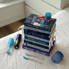 a stack of books sitting on top of a bed next to some pens and markers