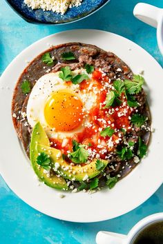 an egg is on top of a tortilla topped with avocado and cilantro