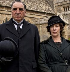 two people standing next to each other in front of a building