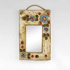 a decorative mirror hanging on a rope with flowers and leaves painted on the frame, in front of a white background