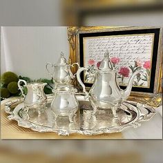 an ornate silver tea set on a tray in front of a framed photo and flowers