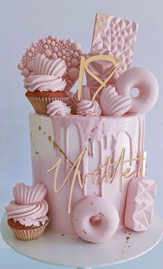 a pink and gold birthday cake with cupcakes on top