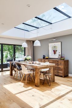 a dining room table and chairs in front of a large window with an open skylight