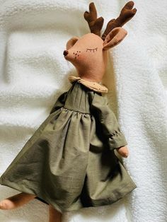 a stuffed animal is laying on a white blanket and wearing a green dress with antlers