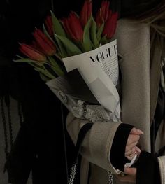 a woman holding a bouquet of red flowers in her left hand and a cell phone in her other hand