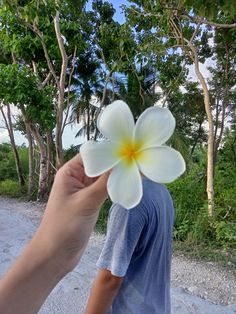 a person holding a flower in front of their face with trees in the back ground