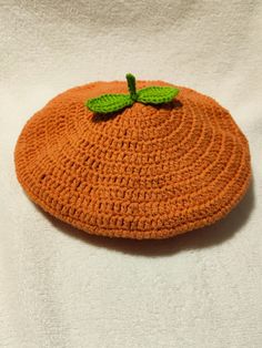 an orange crocheted hat with a green leaf on it sitting on a white surface