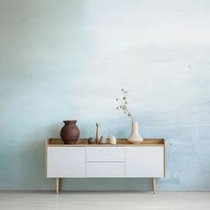 two vases are sitting on top of a white cabinet in front of a blue wall