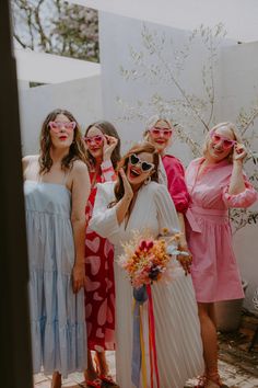 a group of women standing next to each other in front of a white wall wearing sunglasses