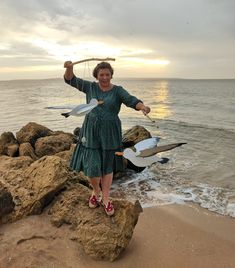 a woman standing on top of a beach next to the ocean holding two white birds