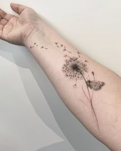 a woman's arm with a dandelion tattoo on it and a butterfly flying away