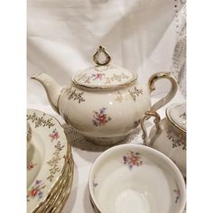 a tea set is sitting on a white tablecloth with floral designs and gold trimmings