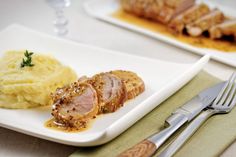 a white plate topped with meat and mashed potatoes next to a fork on a table